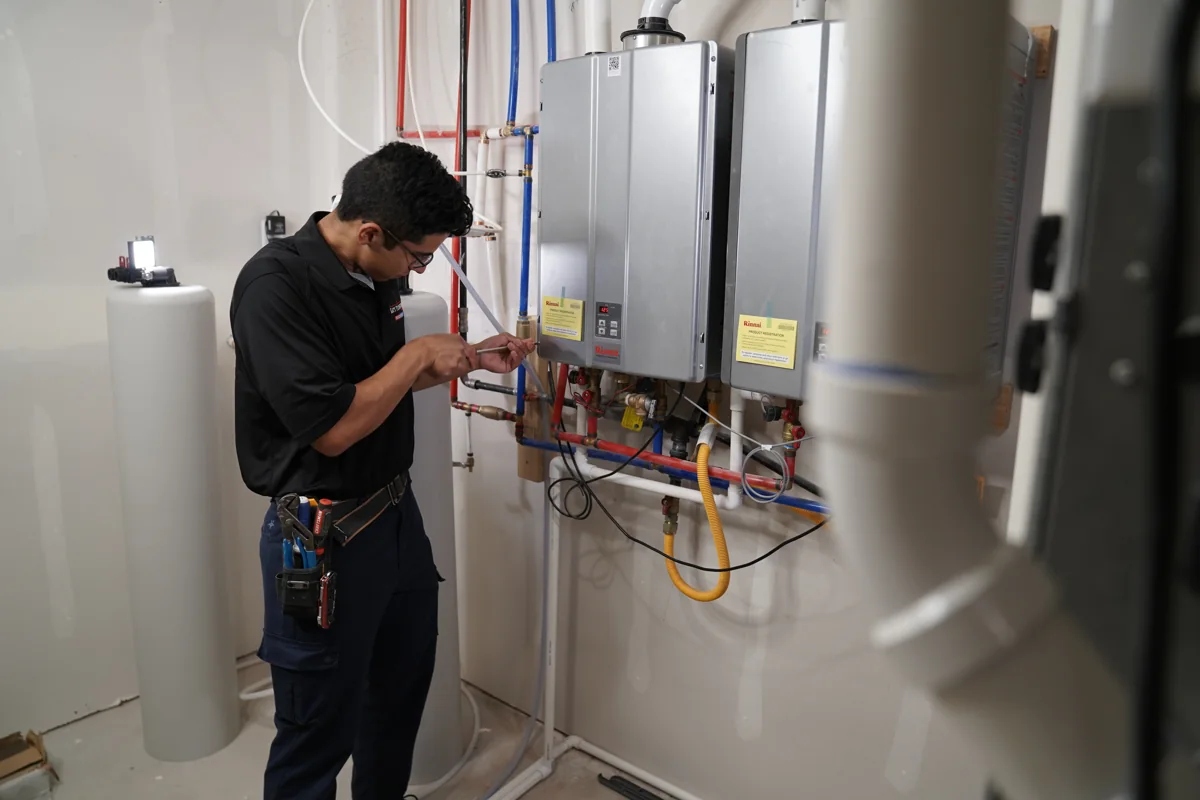 Technician working beside two wall-mounted tankless water heaters with visible plumbing connections
