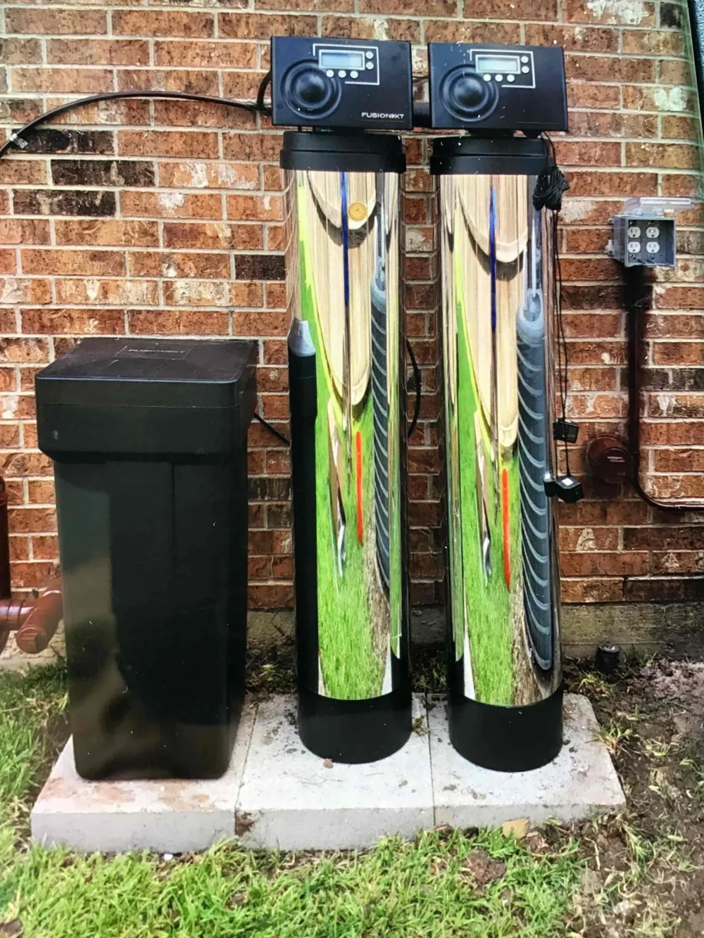Two water treatment tanks and a brine tank beside a brick wall